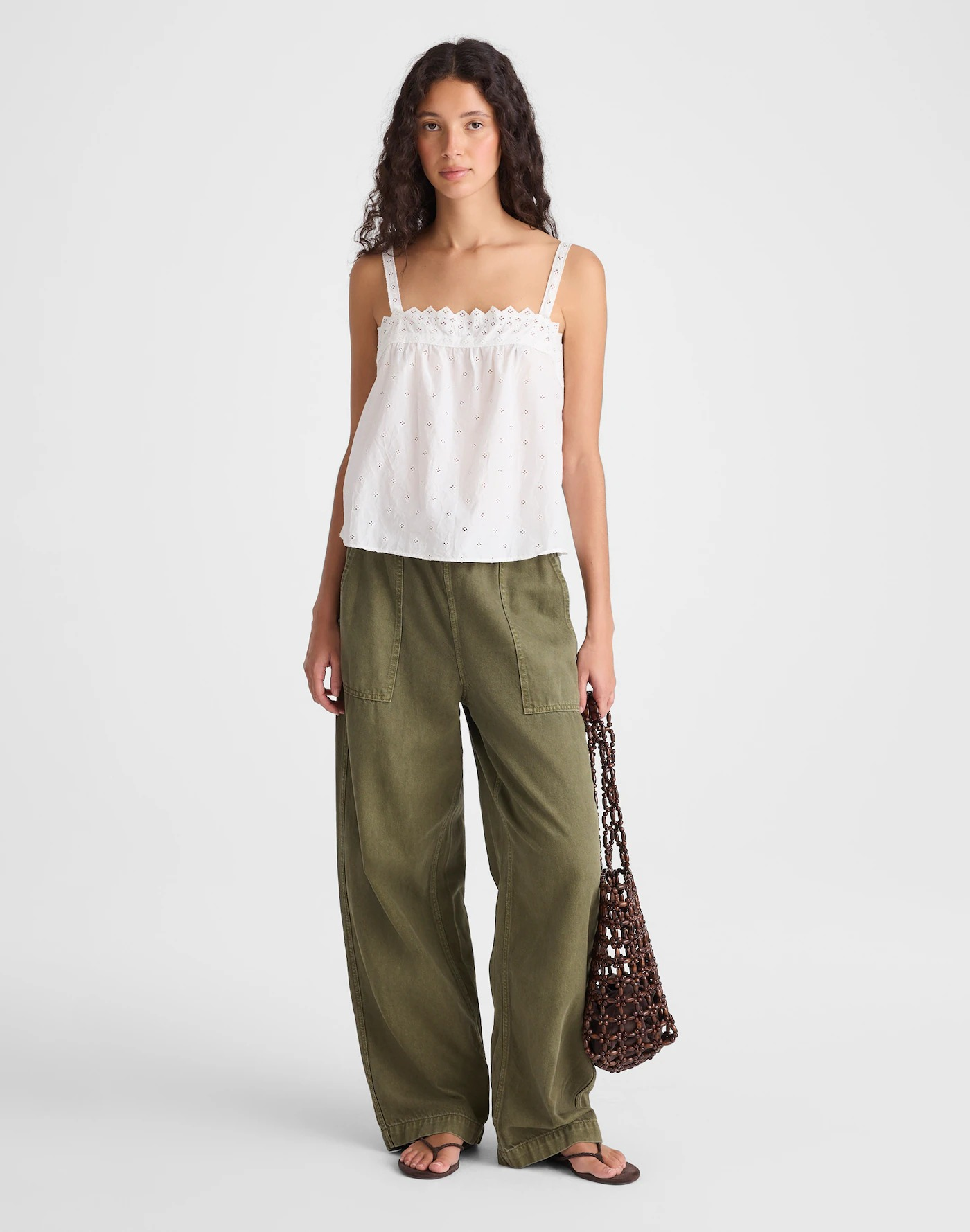 Person wearing a white eyelet sleeveless top and wide-leg pants, holding a net tote bag