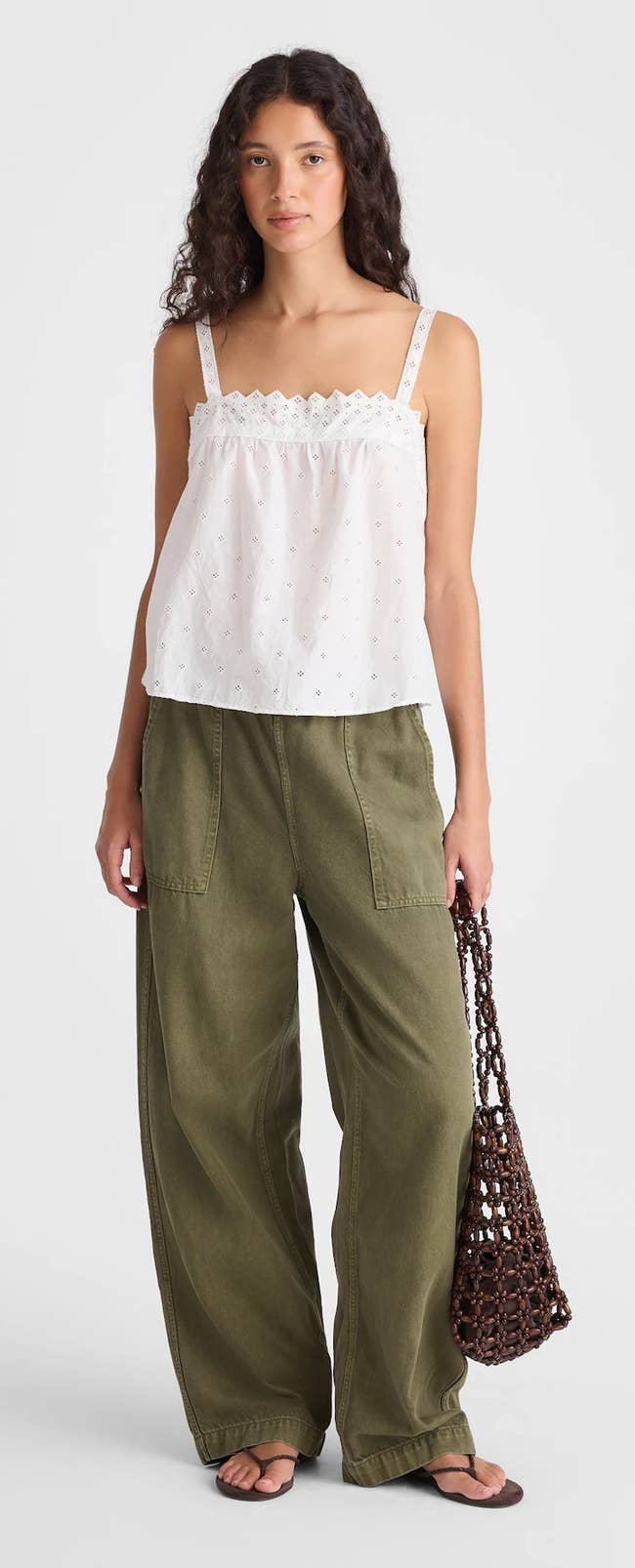 Person wearing a white eyelet sleeveless top and wide-leg pants, holding a net tote bag