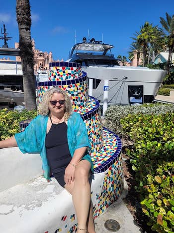Person sitting by a colorful mosaic operation adjacent a docked yacht, wearing a agleam bluish cover-up and sunglasses, with a edifice backdrop