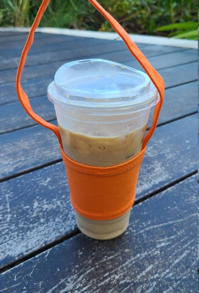 a plastic iced coffee cup in an orange sleeve with a strap 