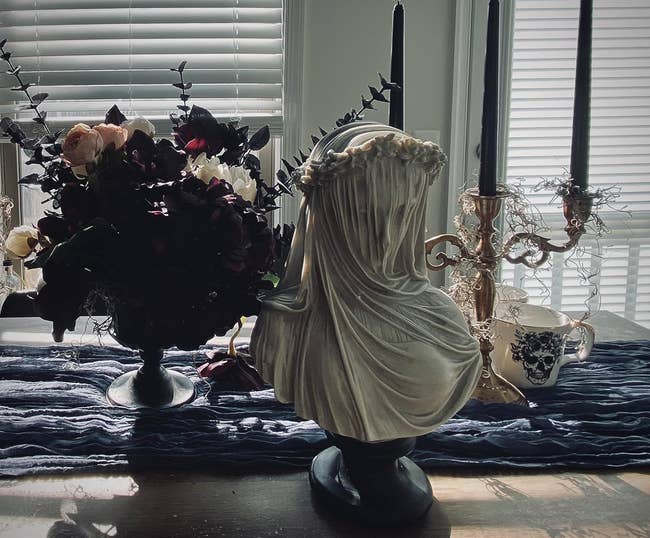 Veiled sculpture on table with decorative flowers and candle holder, giving a classic interior decor vibe