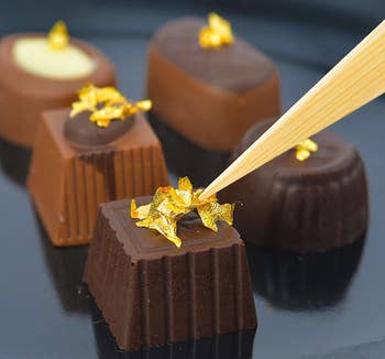 closeup of chocolates with gold leaf being placed on top of each piece