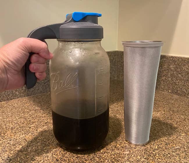 Reviewer holding mason jar filled with cold brew and a spout cap next to silver filter