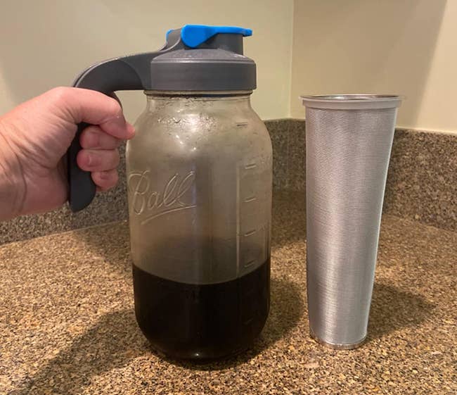 Reviewer holding mason jar filled with cold brew and a spout cap next to silver filter