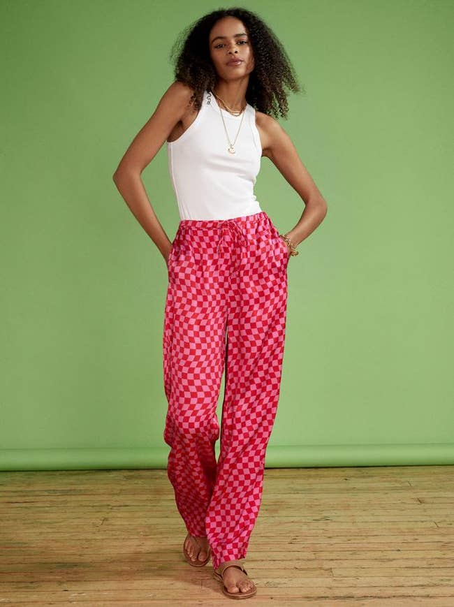 Model wearing bright pink checkerboard trousers with tan sandals and a white tank top