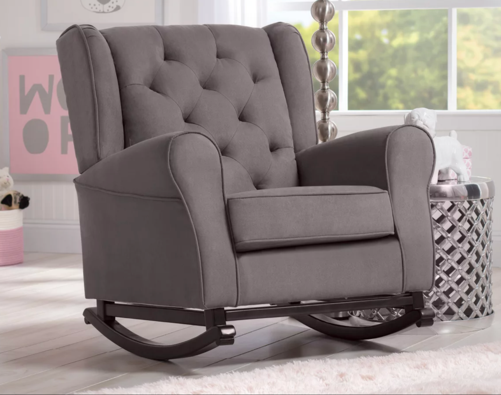 Gray plush rocking chair with rounded armrests and a tufted backing with metal curved legs on hardwood floor