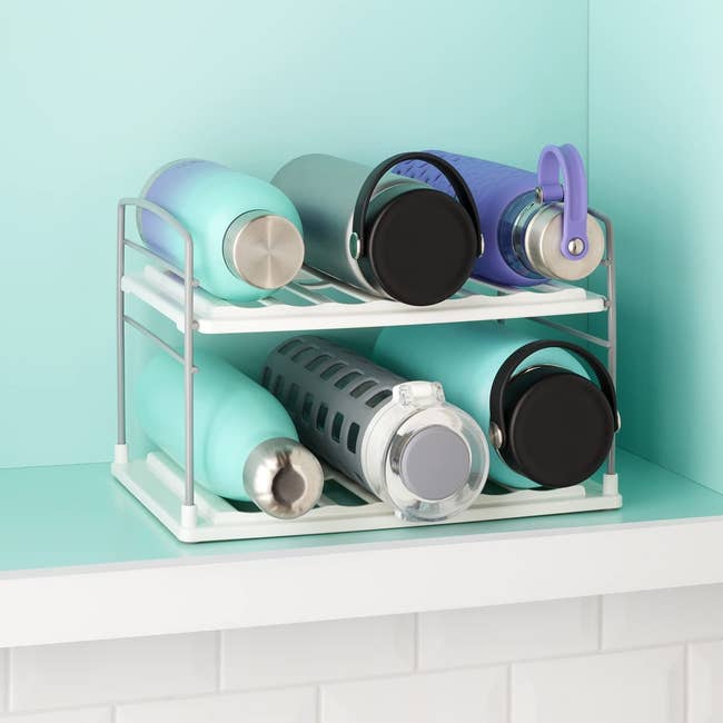 A two tiered wired organizer holding six water bottles in a cabinet 
