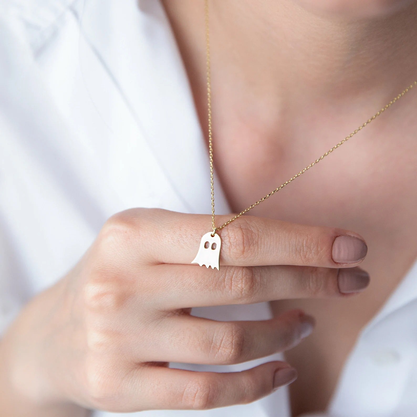 a model holding a gold ghost necklace pendant 