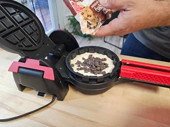 Person adding chocolate chips to batter in a waffle iron for delicious homemade waffles
