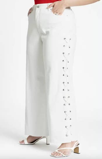 Person modeling white pants with side lace-up details and heeled sandals, focus on fashion style