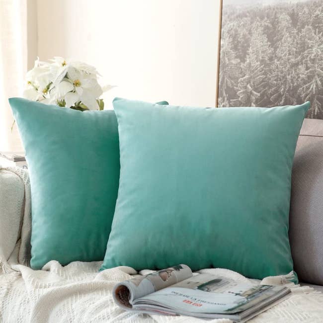 two throw pillows on a couch with aqua green covers on them