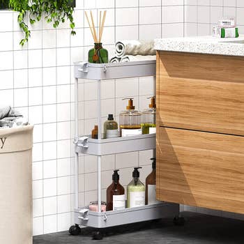 Three-tiered grey storage cart placed between wall and bathroom counter