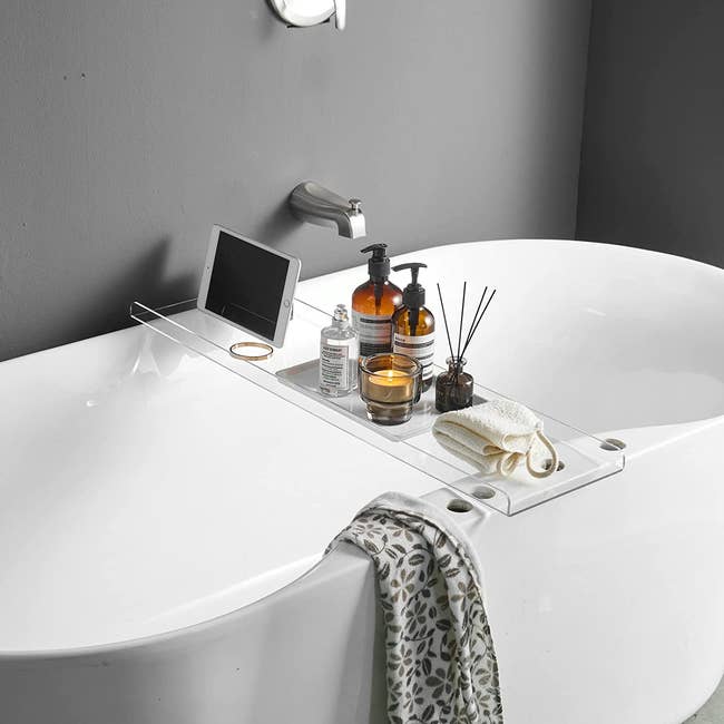 acrylic bathtub caddy holding an ipad, perfume, soap, candle, and diffuser