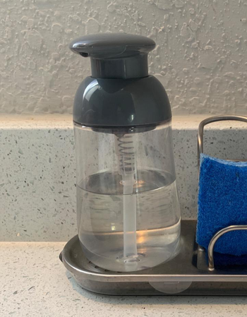 Reviewer image of gray and clear soap dispenser with clear soap next to blue sponge