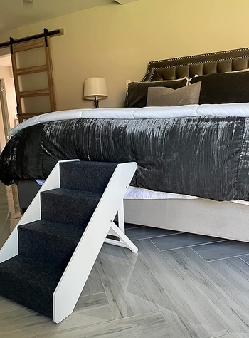 Reviewer image of navy and white wooden pet stairs with adjustable height bar connected to a bed on hardwood floor