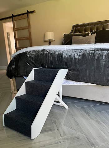 Reviewer image of navy and white wooden pet stairs with adjustable height bar connected to a bed on hardwood floor