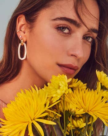 Close-up of a person holding yellow flowers, wearing hoop link earrings