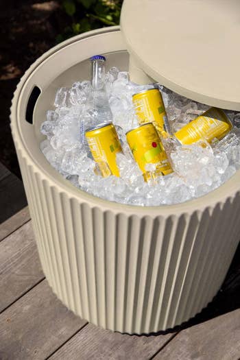 Cooler instrumentality  filled with ice, holding yellowish  cans and a solid  bottle, connected  a woody  deck, suggesting a setup for outdoor refreshments