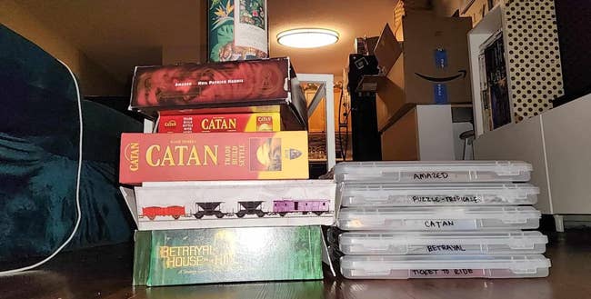 Stack of committee  games, including Catan and Betrayal House connected  the Hill, alongside organized crippled  boxes connected  shelves successful  a room