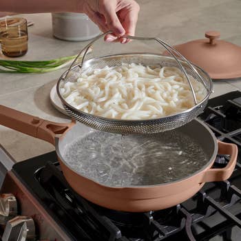 Person draining pasta using a strainer over a pot on a stove