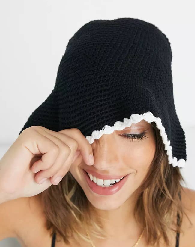Model pulling down front of black crochet bucket hat with white edge