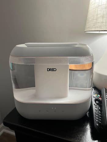Dreo humidifier connected  a table, adjacent  to a distant    and nether  a lamp, showcasing its sleek, modern   design
