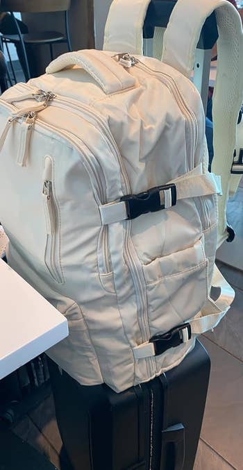 A reviewer's beige backpack on top of their suitcase