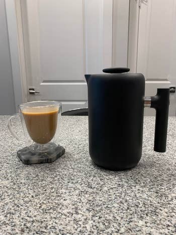 the coffee press next to a cup of coffee it made