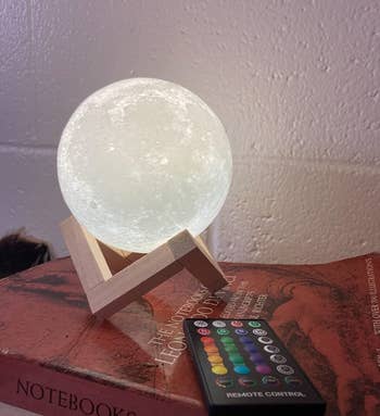 the white glowing moon lamp on a wooden stand next to the remote