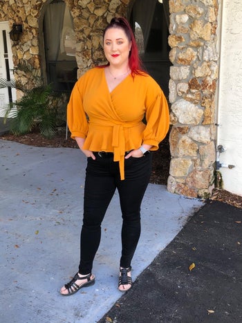 reviewer wearing the dark wash jeans with an orange wrap top