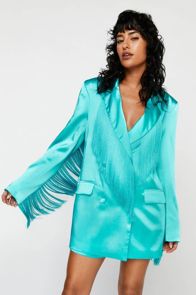 model in teal double breasted satin blazer with fringe on back, sleeves, and lapel worn closed like a dress