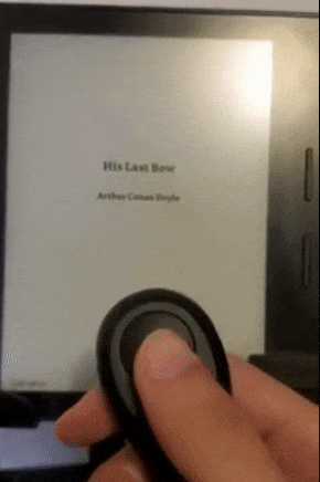 Reviewer using the small black remote to turn pages on a Kindle 