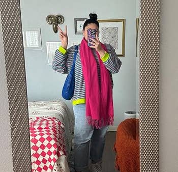 Person successful reflector selfie wearing striped top, jeans, boots, agleam pinkish scarf, with hairsbreadth successful bun, holding phone, bluish container connected shoulder, successful stylish room