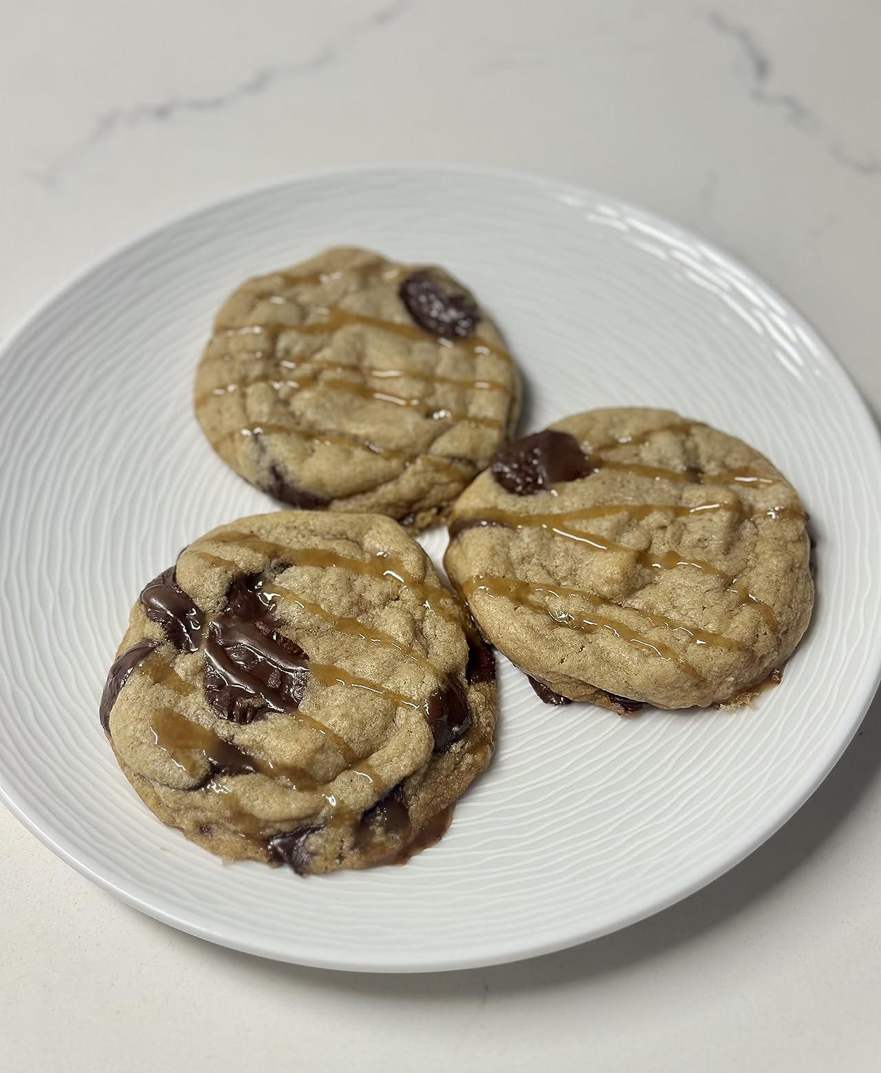 Three cocoa  spot   cookies with caramel drizzle connected  a achromatic  plate