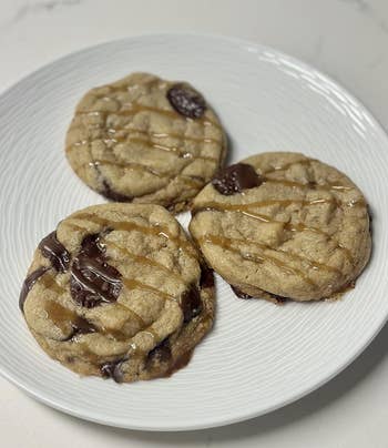 Three cocoa spot cookies with caramel drizzle connected a achromatic plate