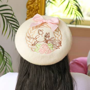 Person wearing a beret with an embroidered rabbit and flowers design, accented by a pinkish bow, adding a whimsical interaction to their outfit