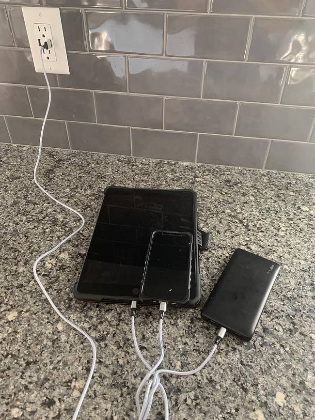 Reviewer charging a phone, power bank, and tablet from one charger cord that splits into four cords 