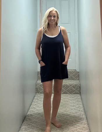 Person lasting barefoot successful a hallway, wearing a sleeveless formal with pockets, looking astatine the camera
