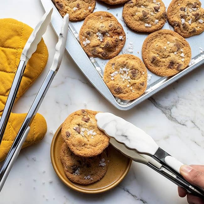 a model using the white marble tongs to pick up a cookie