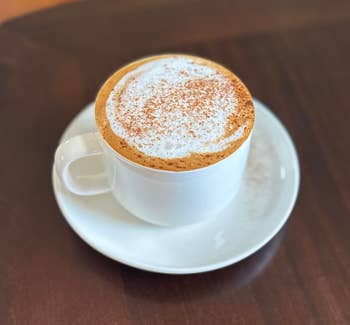 A frothy cappuccino topped with sprinkled cocoa successful a achromatic cupful and saucer connected a woody table