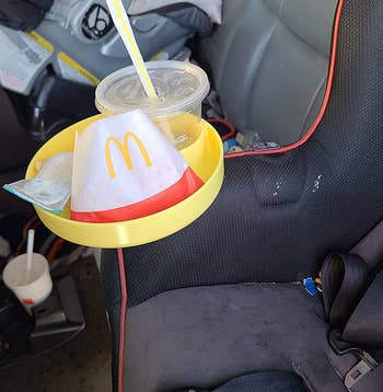 The tray in a carseat cupholder filled with takeout food from McDonald's