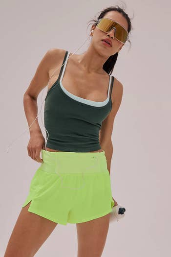 Person in activewear with sunglasses, holding a water bottle, wearing a fitted tank top and shorts, suggesting a sporty, casual shopping theme