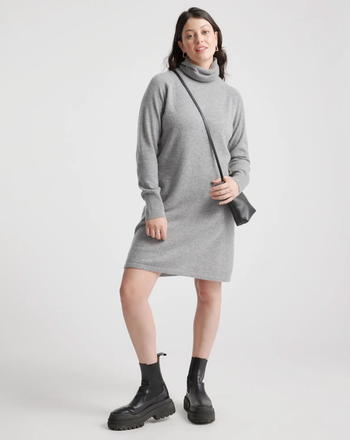 a model wearing the dress in heather grey paired with a black bag and ankle boots