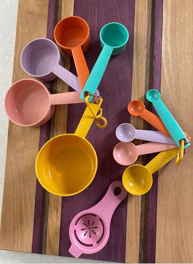 A set of colorful measuring cups and a citrus juicer on a wooden board
