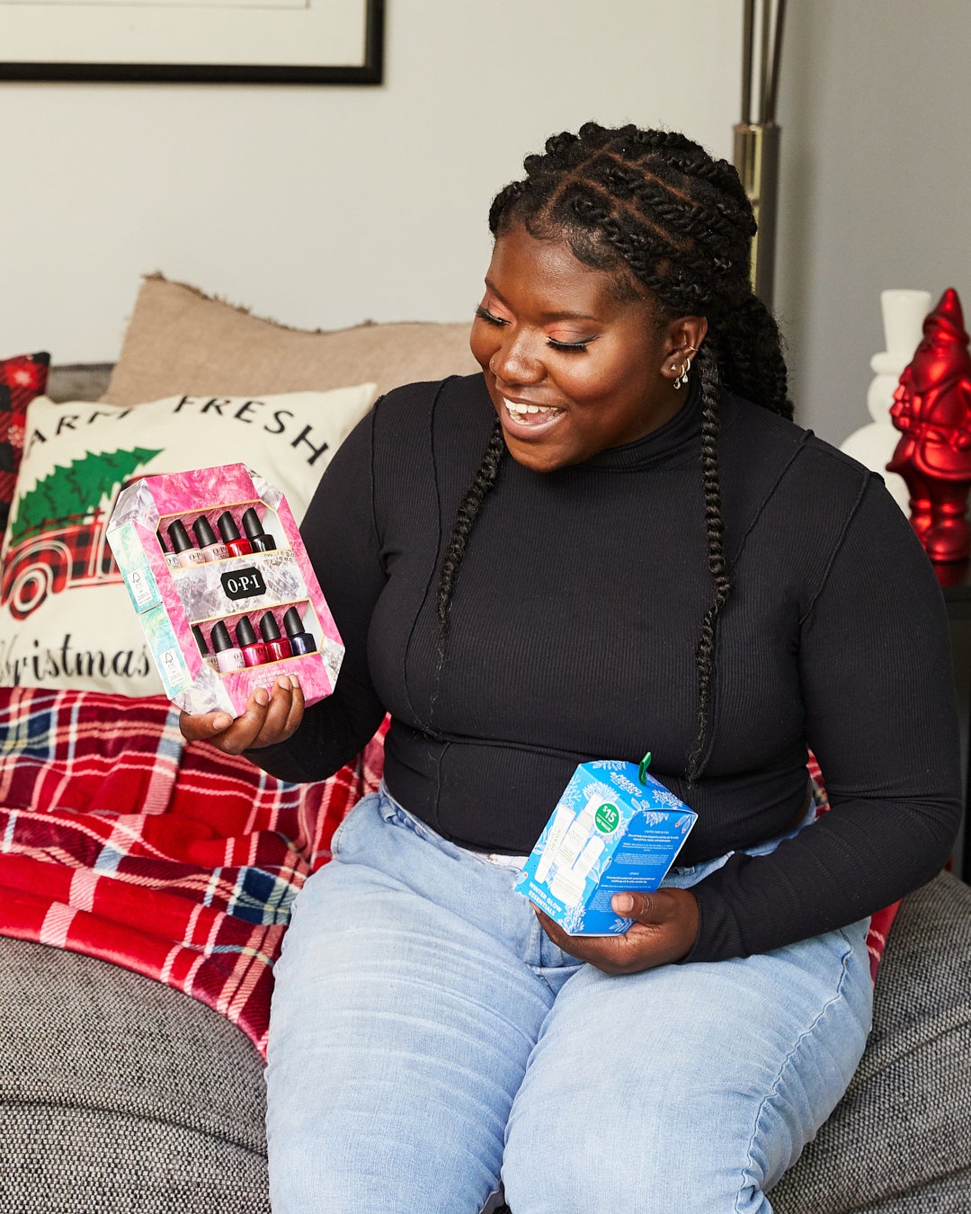Elise holding OPI holiday nail polish and winter glow essentials beauty kit on couch