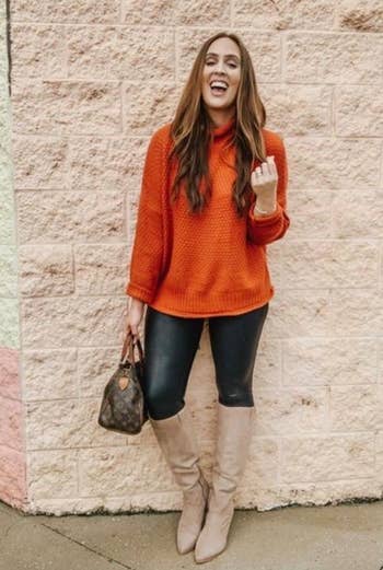 reviewer wearing batwing sleeve sweater in an orange color with jeans and knee-high boots