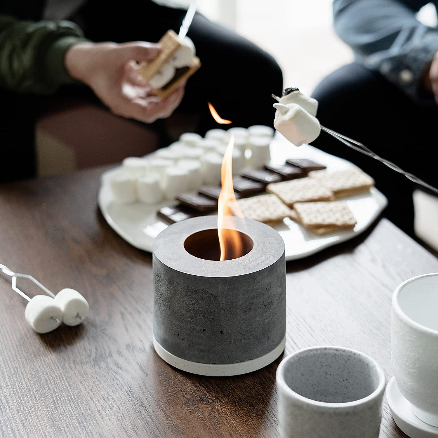 the personal fireplace on top of a coffee table next to s'mores ingredients while people heat marshmallows over the flame