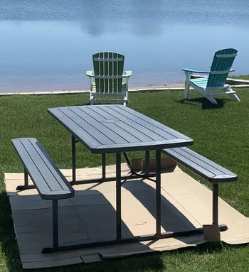 reviewer photo of the gray table and benches on a lawn near a lake