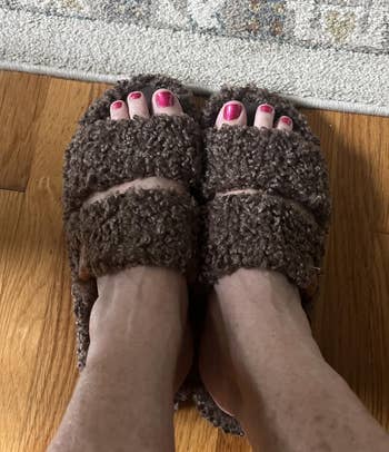 Person wearing cozy, plush slippers with pinkish toenails, lasting connected a woody level and a patterned rug