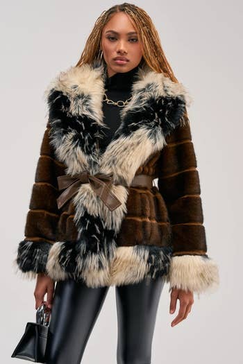 Person wearing a fur overgarment with a belt, sleek pants, and holding a tiny handbag, suitable for a manner buying article